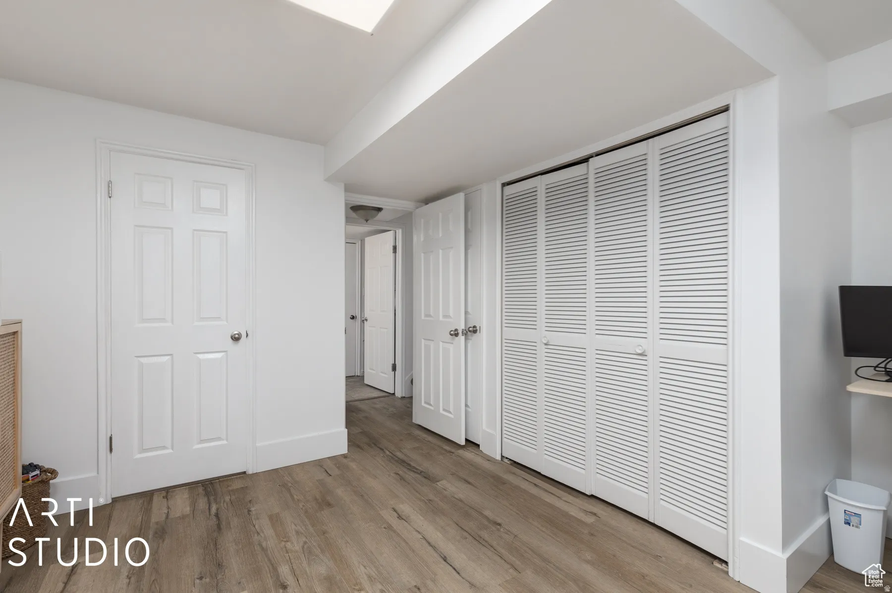 Room featuring wood-finish flooring, white walls, and a white six-panel door