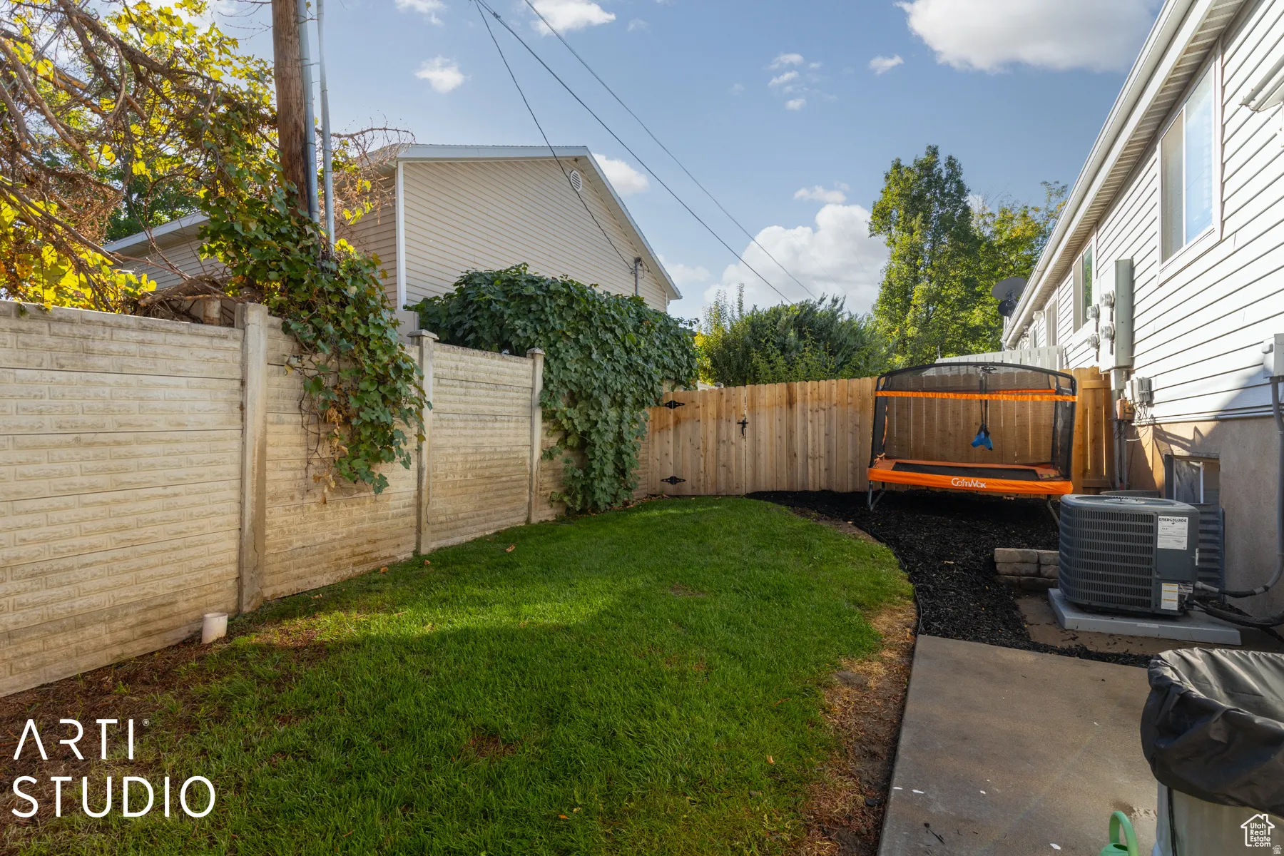 Fenced backyard featuring a manicured lawn, concrete patio, and mature landscaping