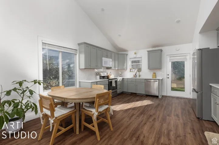 Vaulted ceiling kitchen featuring wood-finish flooring, shaker-style cabinetry, white subway tile backsplash, and stainless steel appliances