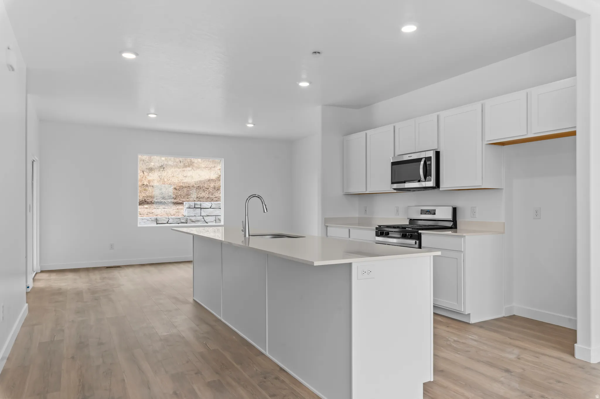 Open-concept kitchen featuring white shaker cabinetry, stainless steel appliances, and a central island with an integrated sink