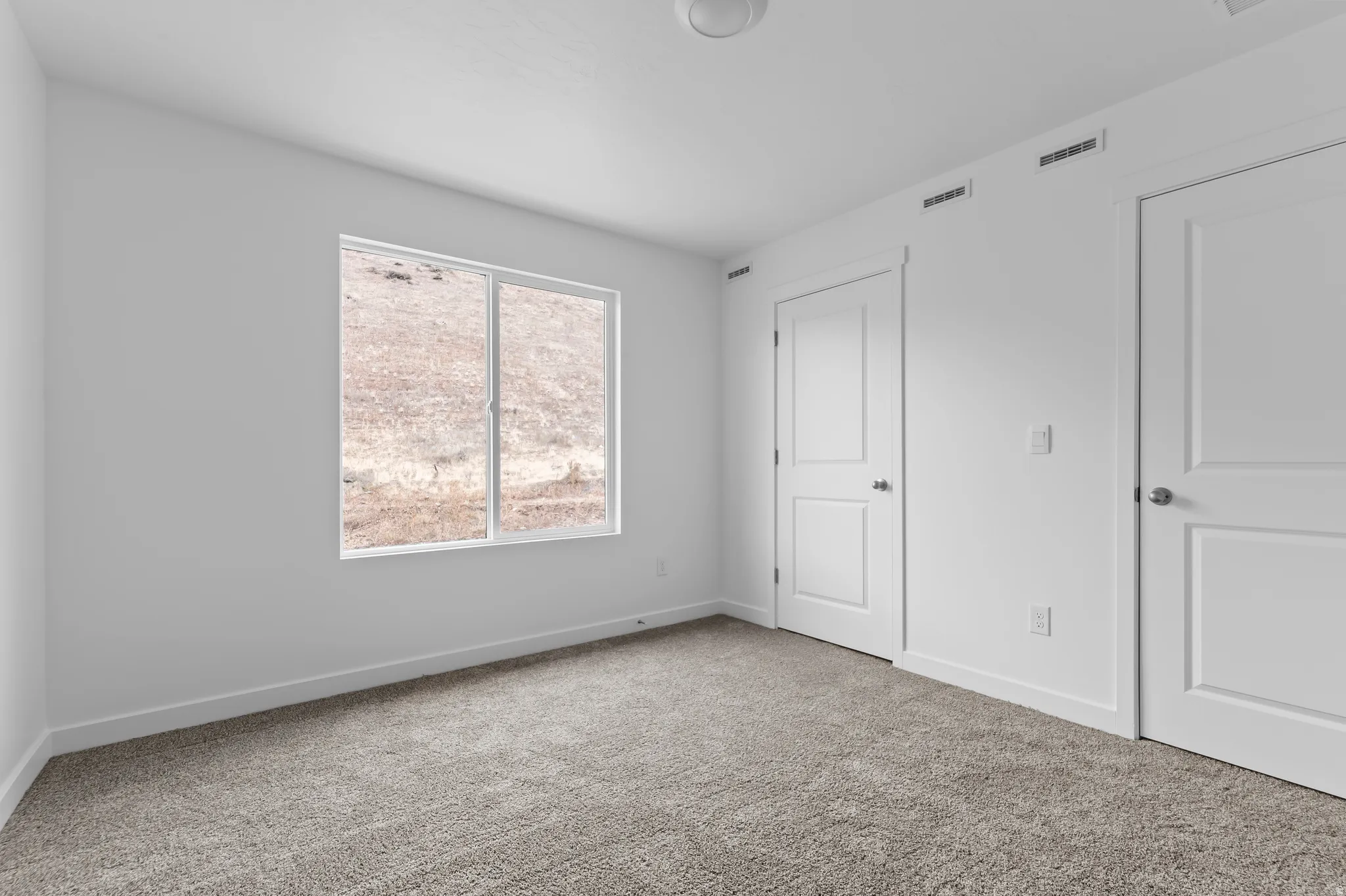 Neutral toned carpeting, white walls, and bright window with surrounding natural scenery