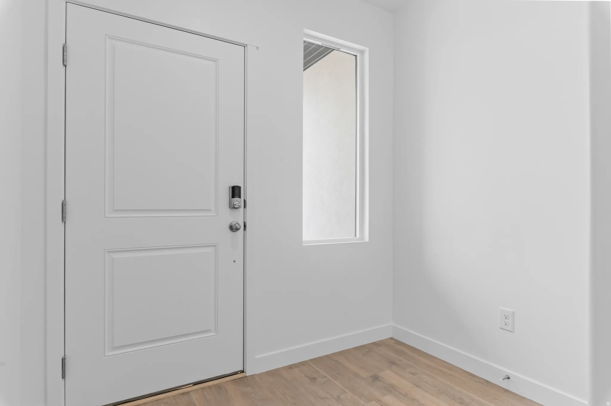 Entryway featuring a white paneled door with smart lock, light wood-finish flooring, a tall transom window, and crisp white walls