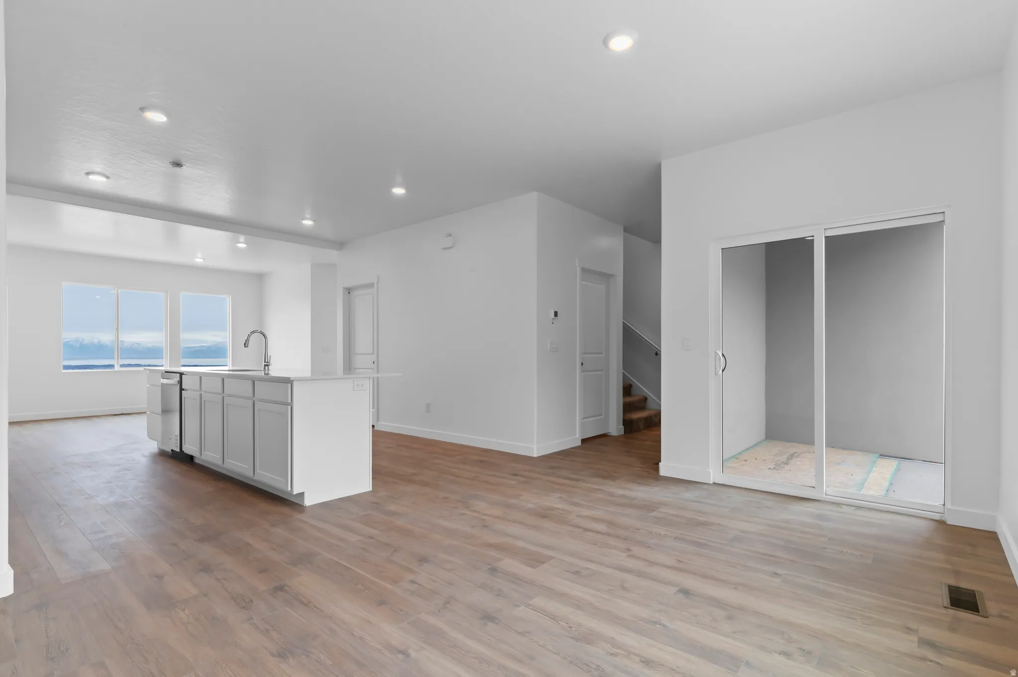 Spacious open-concept interior featuring wood-finish flooring, a contemporary kitchen island with a stainless steel sink, recessed lighting, and large windows