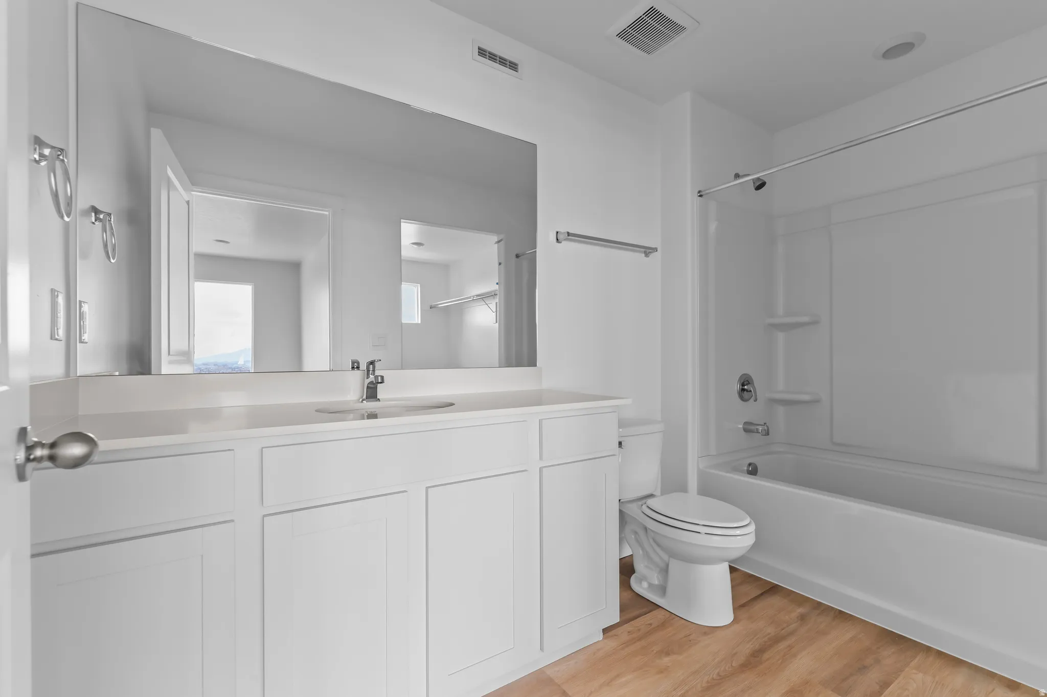 Bathroom featuring a white vanity with an integrated sink, a large wall-mounted mirror, and a combination tub/shower with white surround