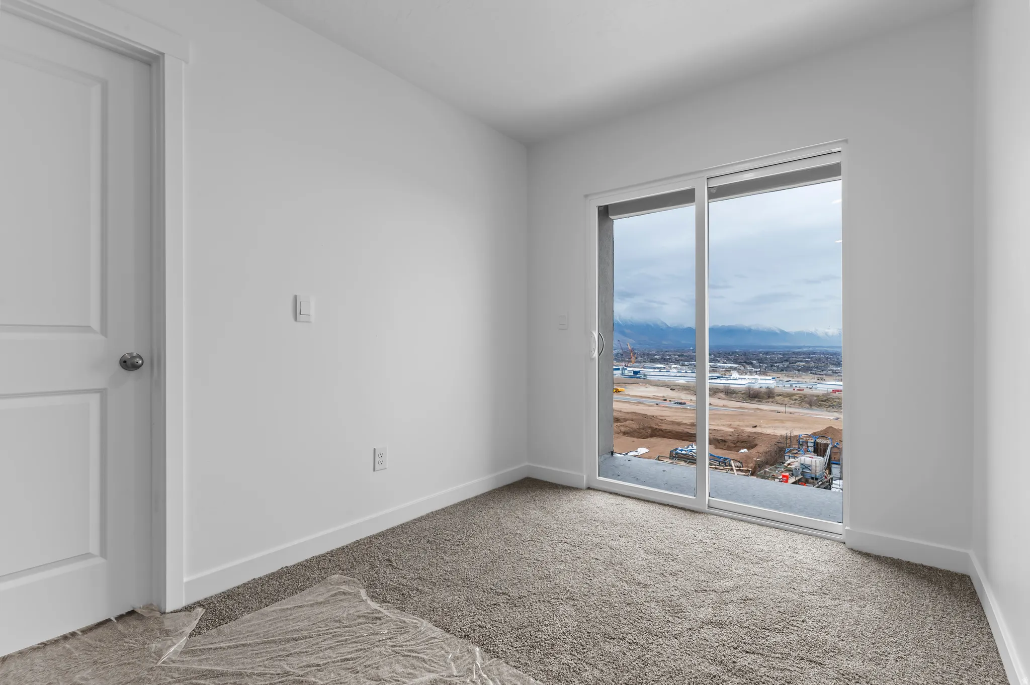 Room featuring a sliding glass door with a mountain backdrop, white walls, white baseboards, and gray textured carpeting