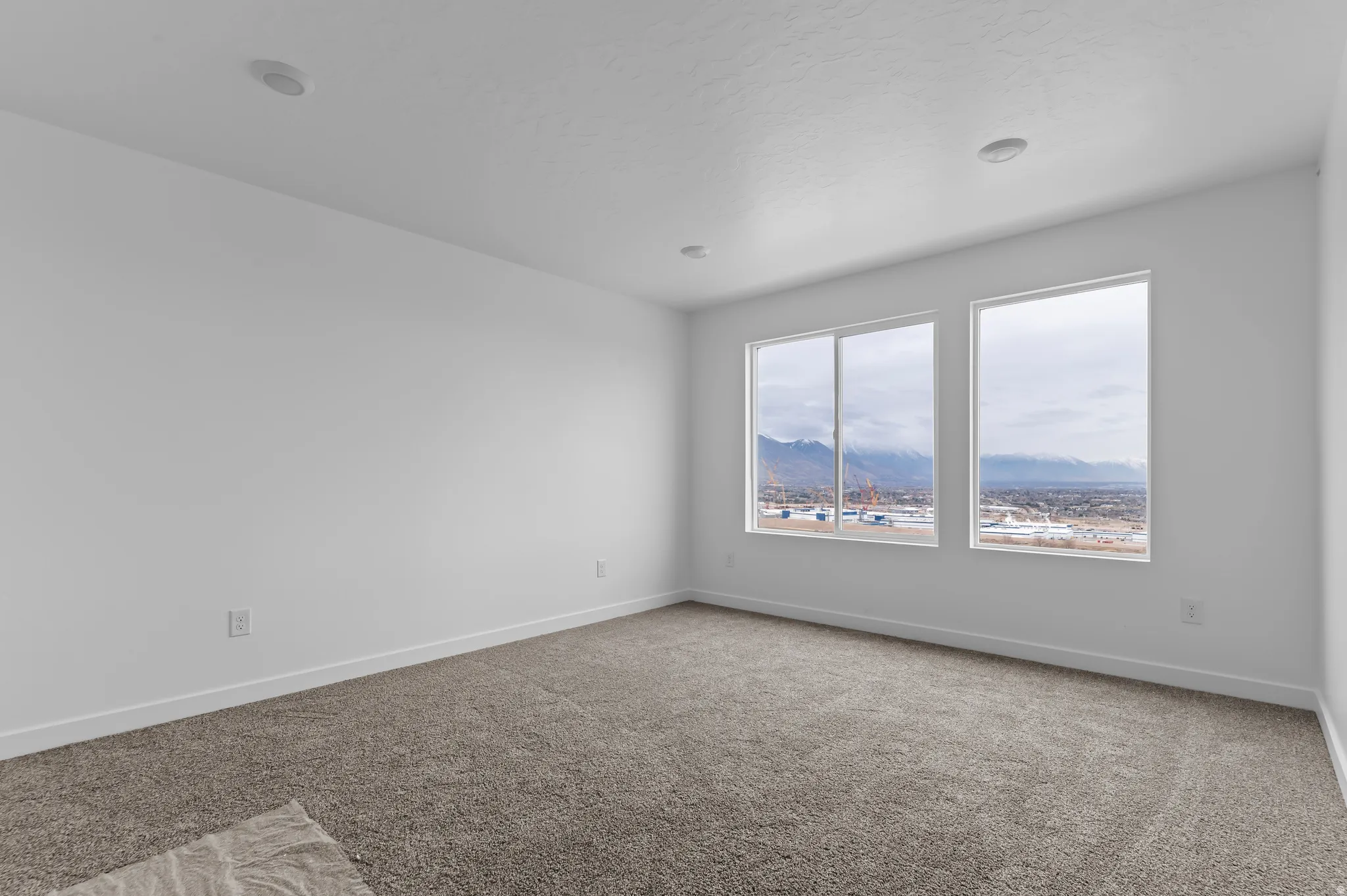 Spacious interior room featuring three large windows, recessed ceiling lighting, light-colored walls, thick baseboard trim, and plush carpet flooring