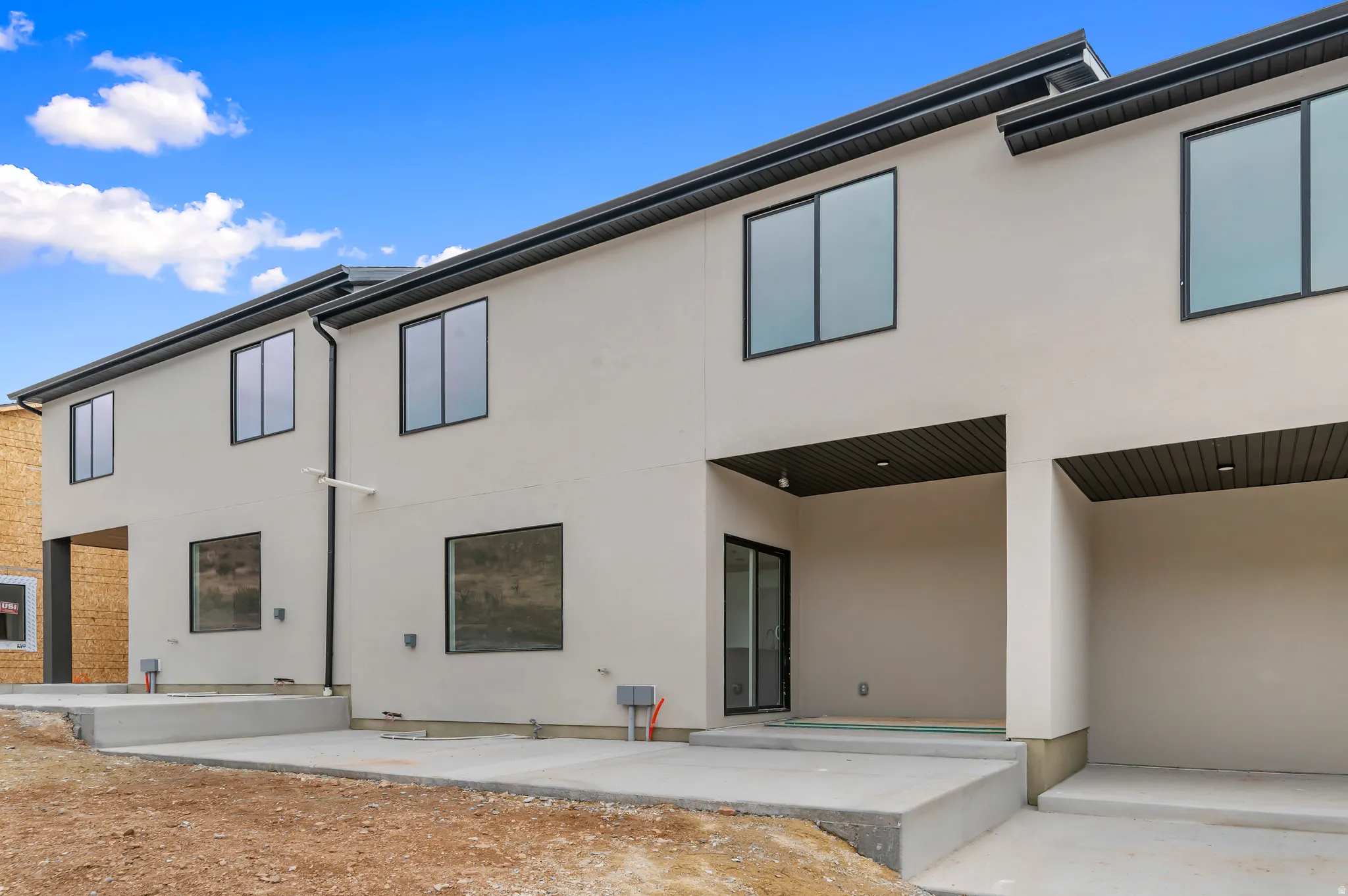 Modern exterior featuring light-colored stucco, dark-framed windows, and a dark soffit
