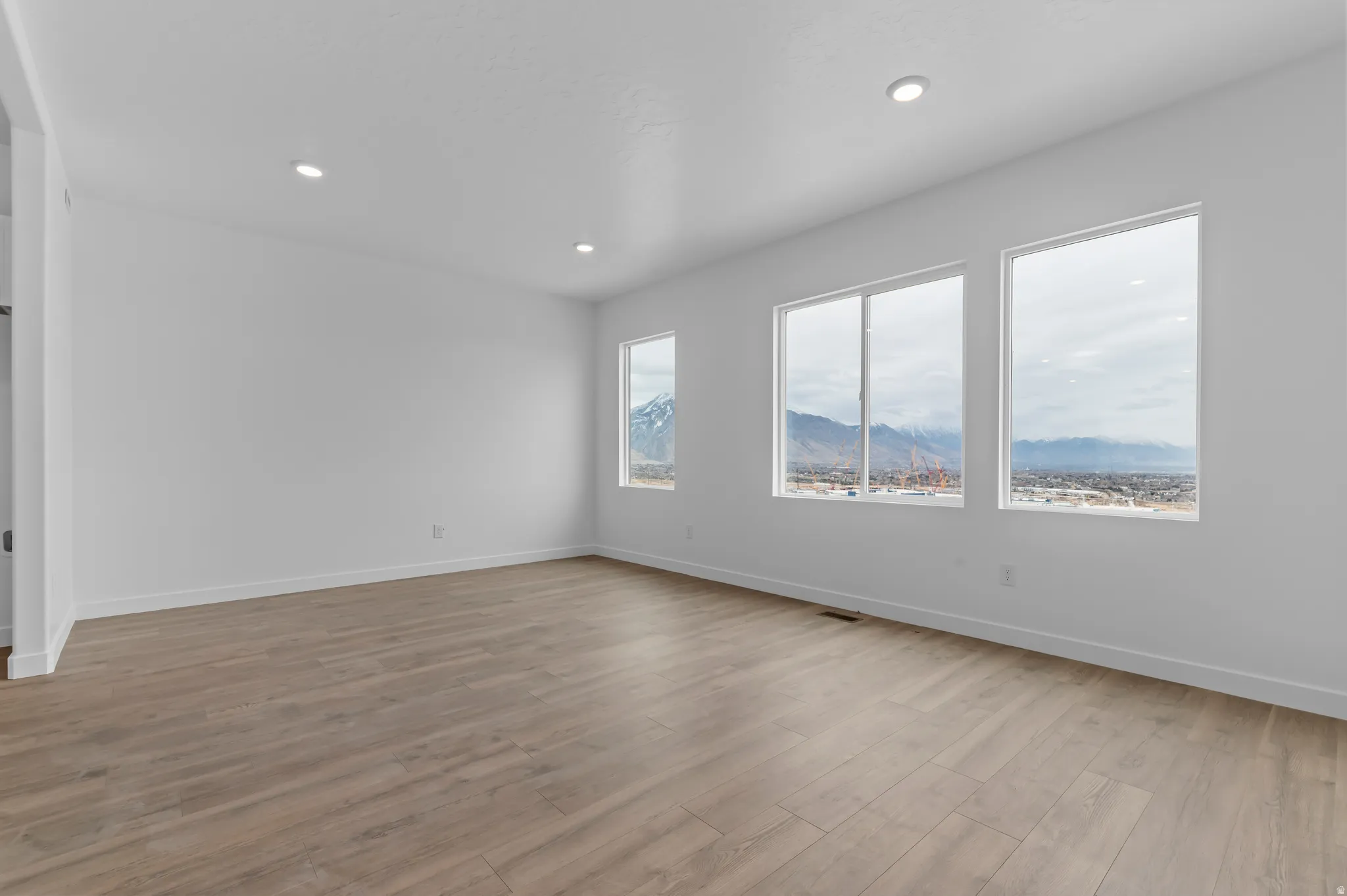 Spacious interior with wood-finish flooring, recessed lighting, and large windows showcasing a mountain backdrop