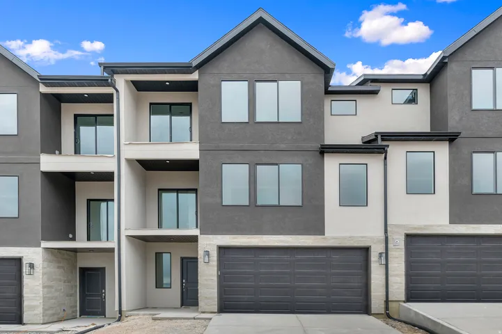 Modern multi-level townhome featuring a dark gray stucco exterior, light stone accents, and multiple balconies with sliding glass doors