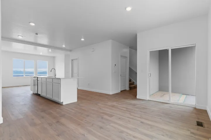 Spacious open-concept interior featuring wood-finish flooring, a contemporary kitchen island with a stainless steel sink, recessed lighting, and large windows