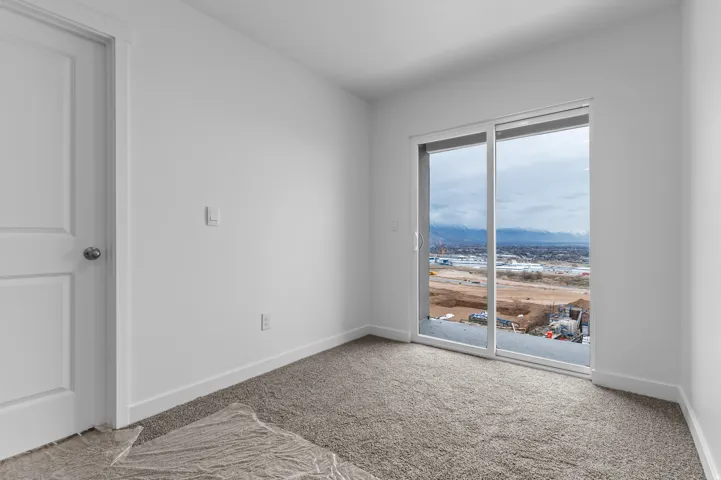 Room featuring a sliding glass door with a mountain backdrop, white walls, white baseboards, and gray textured carpeting