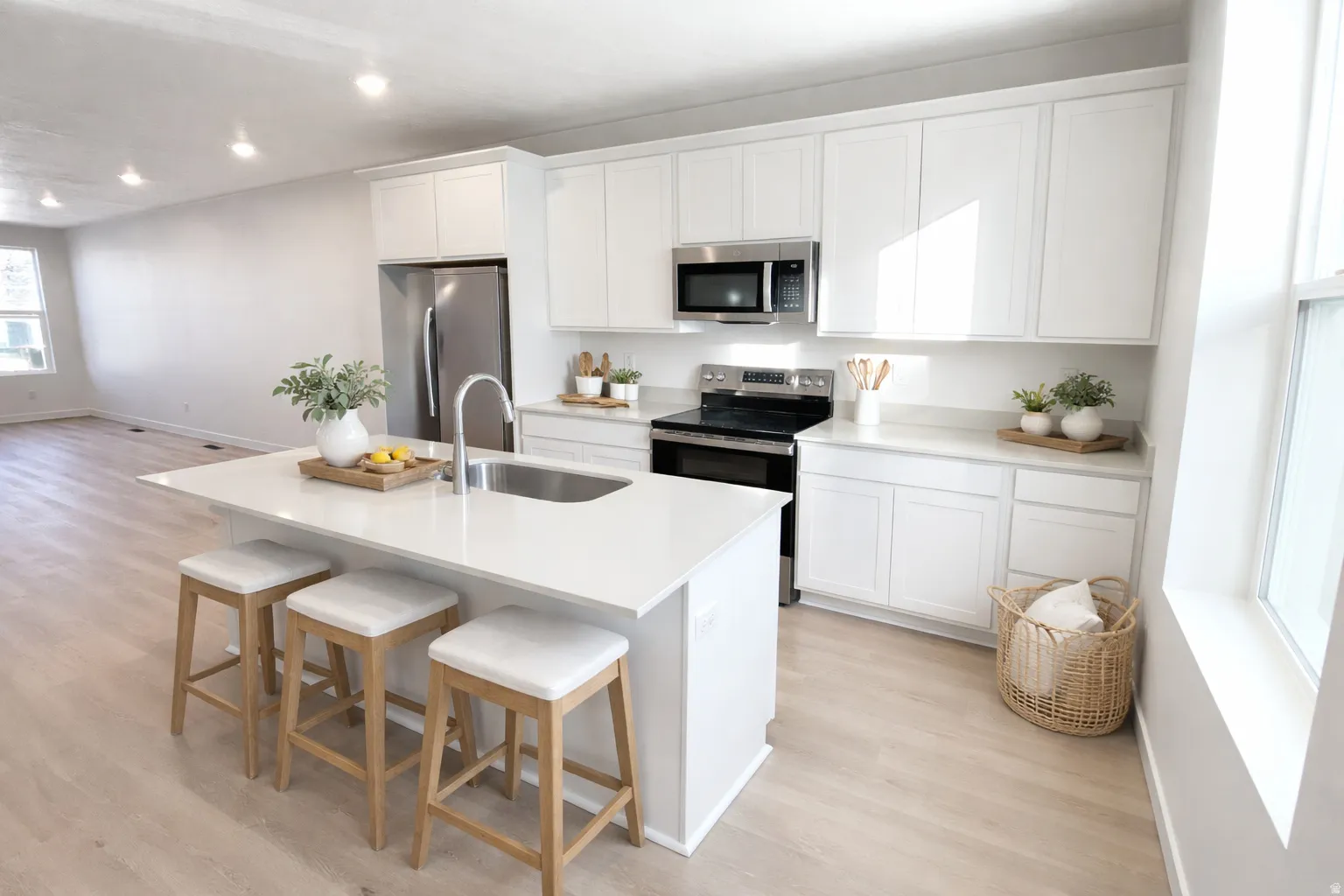 Contemporary kitchen featuring white cabinetry, stainless steel appliances, a center island with integrated sink, light-toned wood-finish flooring, and recessed lighting