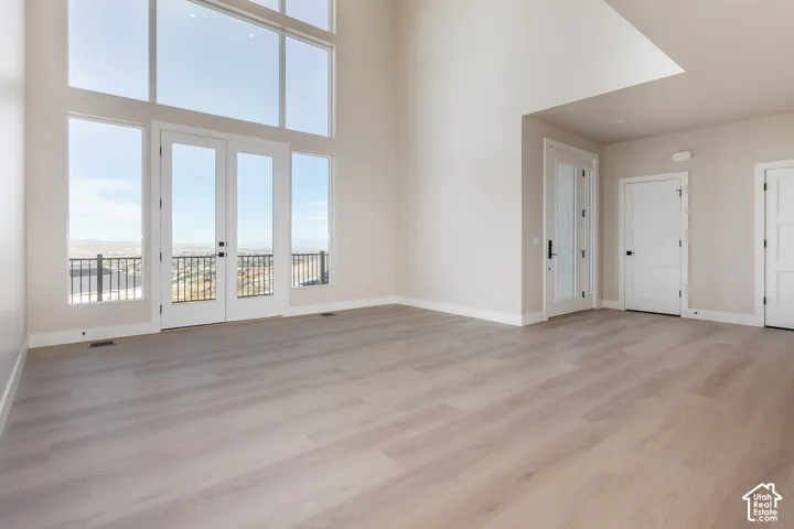 Expansive living area with high ceilings, large floor-to-ceiling windows, and light wood-finish flooring