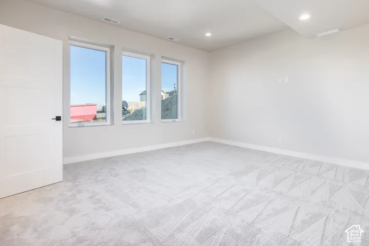 Light gray walls, three vertical windows, patterned carpet, recessed ceiling lighting, and a white paneled door with black hardware