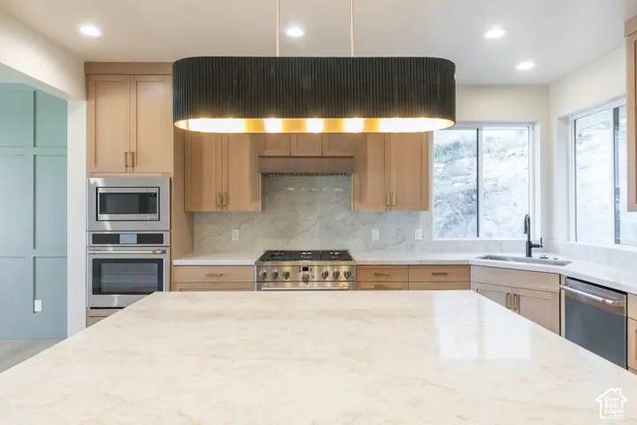 Central kitchen island with stone countertop, natural wood-finish cabinetry, stainless steel appliances, and a black statement pendant light