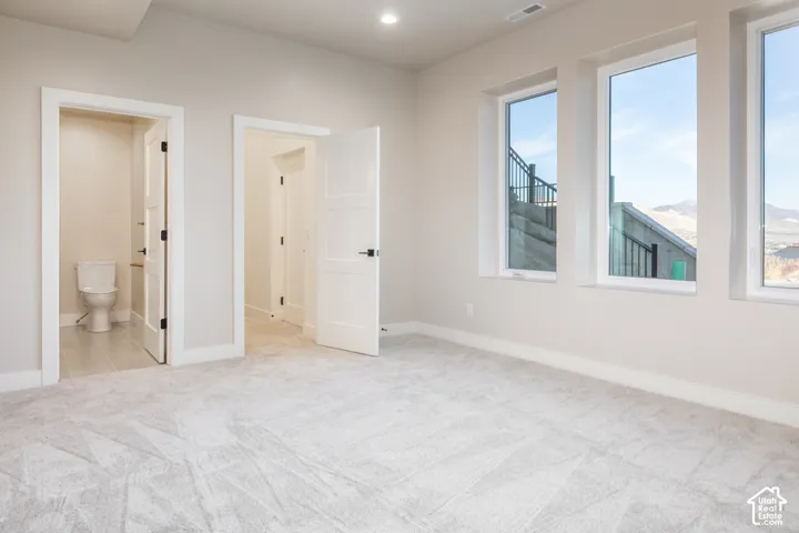 Plush carpeting, three large windows, recessed ceiling lighting, a white toilet with a toilet roll holder, and a flat-panel door with matte black hardware
