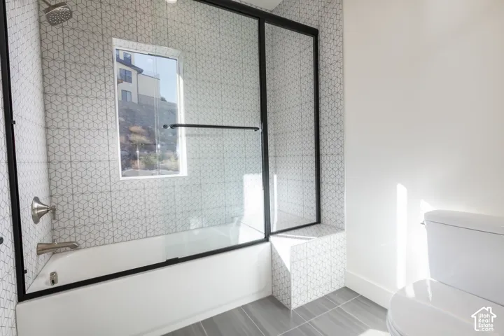 Bathtub with brushed nickel fixtures, geometric tile surround, and a clear glass shower enclosure with matte black framing
