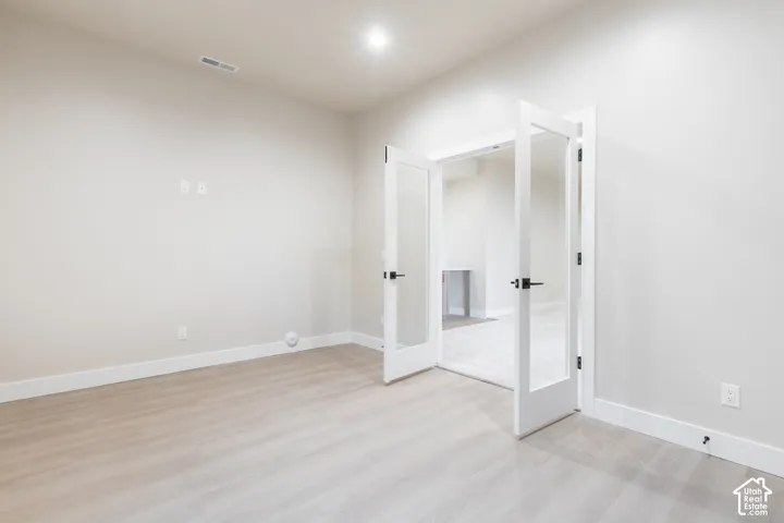 Wood-finish flooring, white walls, recessed lighting, and French doors with black hardware