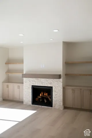 Stone-clad fireplace with a wood-finish mantel, recessed lighting, wood-finish flooring, and built-in cabinetry with open shelving