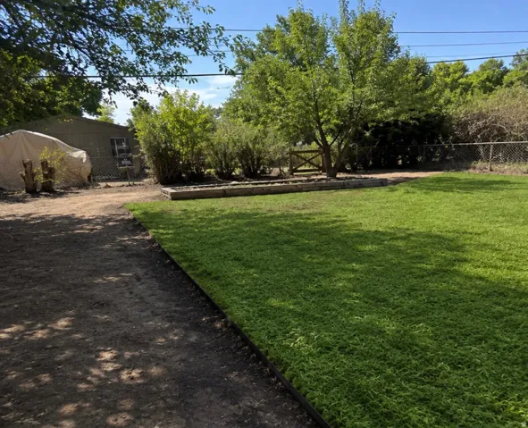 Expansive green lawn with a defined border, gravel path, built-in raised garden beds, mature trees, and a wooden gate