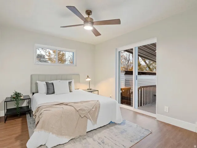 Bedroom featuring wood-finish flooring, a contemporary ceiling fan with integrated lighting, a horizontal window, and a sliding glass door leading to an outdoor deck area