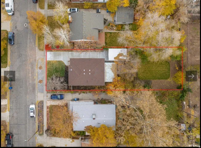 Aerial perspective of a property featuring a single-story residence with a brown shingled roof, a paved driveway, and a front lawn