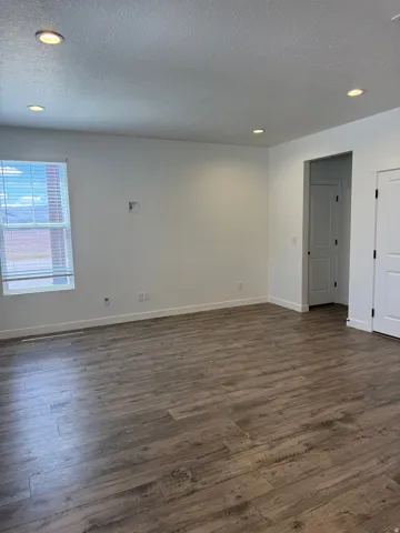 Spacious room featuring wood-finish flooring, recessed ceiling lighting, a large window with horizontal blinds, and crisp white walls