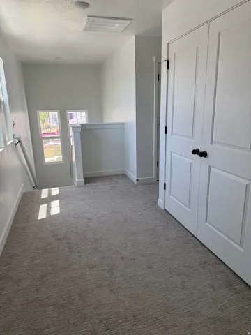 Carpeted upper-level landing featuring a white painted railing, two paneled doors with dark hardware, recessed lighting, and a white ceiling access panel