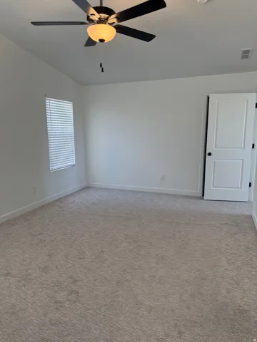 Spacious room featuring neutral carpeting, white walls, a ceiling fan with integrated lighting, a window with horizontal blinds, and a white interior door with dark hardware