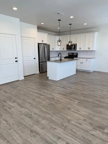 Open-concept kitchen featuring an island with a sink, stainless steel appliances, white cabinetry with dark hardware, and recessed lighting