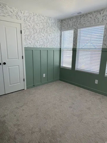 Room featuring light gray patterned carpet, sage green wainscoting, and botanical print wallpaper