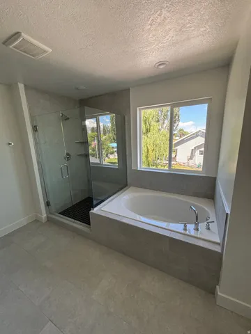 Glass-enclosed shower with dark-tiled floor, built-in bathtub with deck-mounted fixtures, large window, and tile flooring