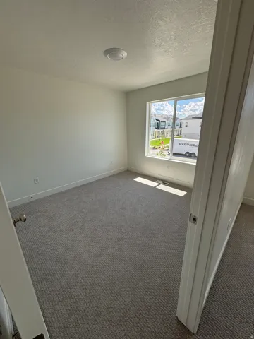 Neutral-toned carpet flooring, recessed ceiling lighting, and a large window with white trim