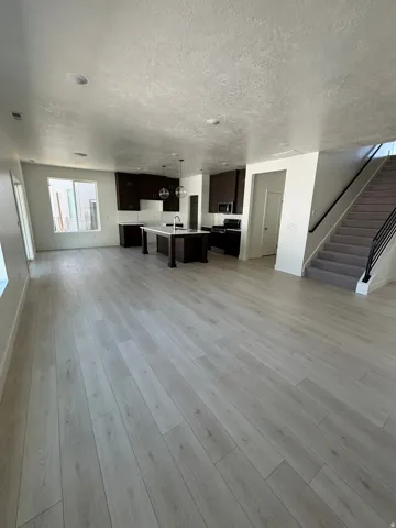 Open-concept living area with wood-finish flooring, a kitchen island, dark wood cabinetry, and a carpeted staircase with a metal railing
