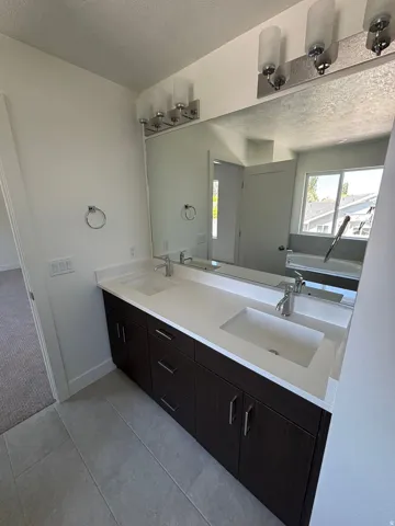 Dual vanity featuring integrated rectangular sinks, white countertops, dark wood-finish cabinetry, and chrome fixtures