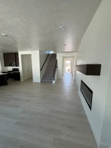 Spacious interior featuring wide plank wood-finish flooring, a built-in electric fireplace, a dark wood-finish mantel, and recessed lighting