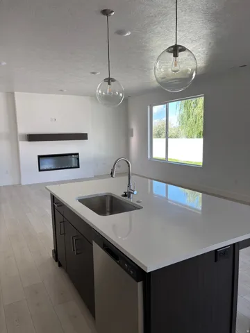 Spacious open-concept living area featuring an eat-in island with an undermount stainless steel sink, sleek stainless steel dishwasher, and two suspended glass pendant lights