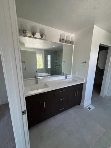 Dual vanity with integrated sinks, dark wood-finish cabinetry, a large frameless mirror, and overhead sconce lighting