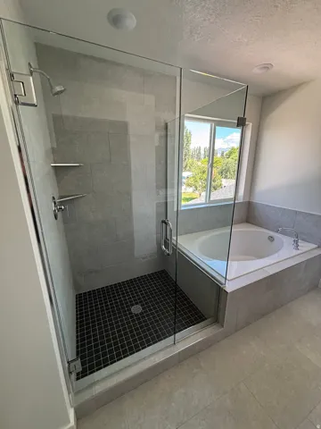 Glass-enclosed shower with gray tiled walls and black mosaic floor