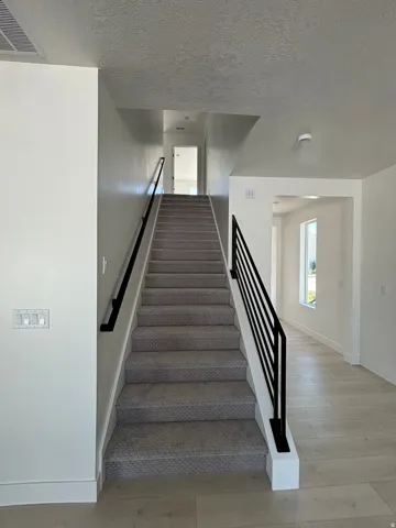 Staircase featuring carpeted treads, metal railings, and wood-finish flooring