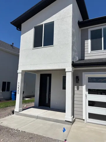 Contemporary exterior featuring a smooth stucco finish, gray horizontal siding, a black front door, a modern garage door with frosted panels, and exterior wall lighting