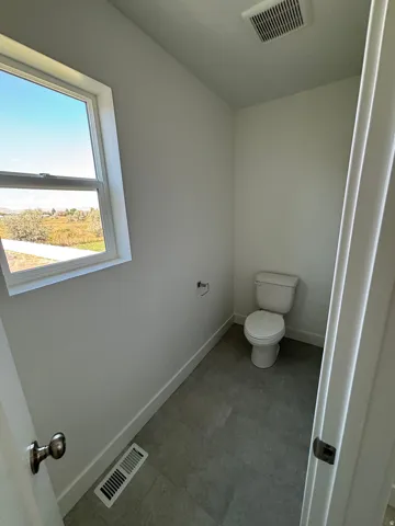 White toilet, window with exterior scenery, tiled flooring, white walls, and white trim