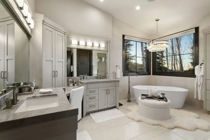 Spacious bathroom featuring a freestanding tub, dual vanities with integrated sinks, ample cabinetry, and large windows with natural scenery