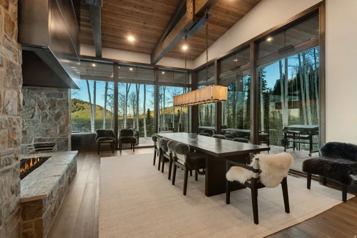 Expansive dining area featuring a full-height stone fireplace, wood-finish flooring, and a vaulted ceiling with exposed beams