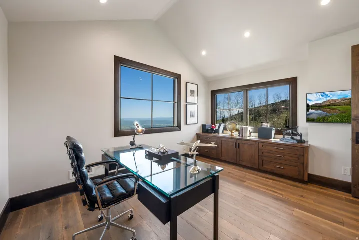 Spacious room featuring vaulted ceilings, recessed lighting, wood-finish flooring, and expansive windows with dark wood frames