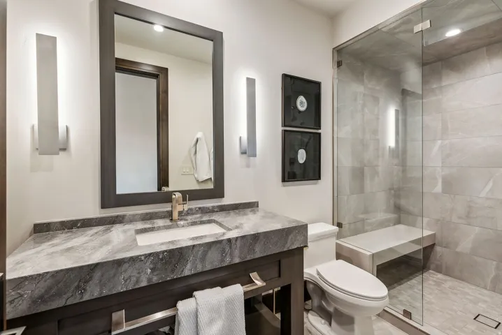 Bathroom featuring a dark wood-finish vanity with a stone countertop and integrated sink, a framed mirror, and contemporary sconce lighting