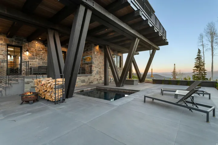 Exterior patio featuring a built-in spa, expansive concrete hardscaping, and a stone-clad facade with dark window frames
