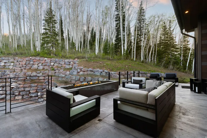 Expansive concrete patio featuring a built-in fire pit, stone retaining wall, and black metal railings