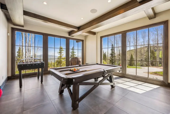 Spacious room featuring multiple large picture windows with dark trim, recessed lighting, exposed ceiling beams, and dark tile flooring