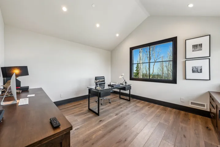 Bright interior space featuring a large window with black framing, wood-finish flooring, a vaulted ceiling, recessed lighting, and dark baseboards